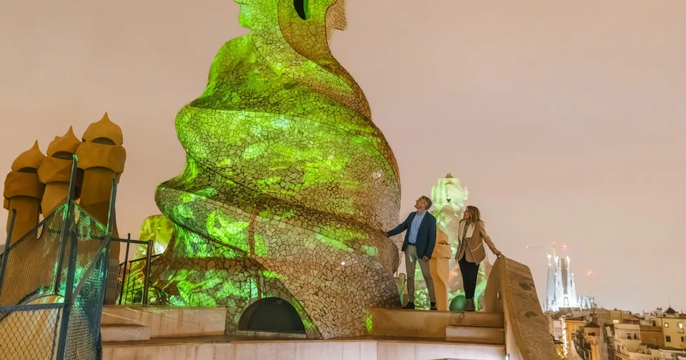 Visitors on a rooftop beside a twisted chimney lit up in green light at dusk